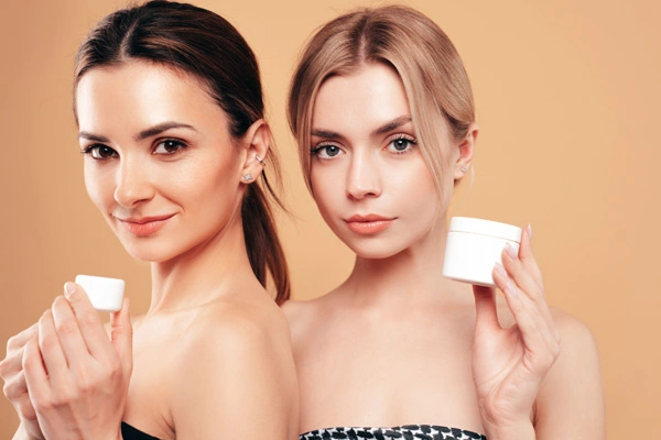 Dwie śliczne młode kobiety prezentują w dłoniach różnego rodzaju kosmetyki z witaminą C